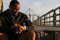Мужчина-спортсмен использует свои умные часы на пирсе на пляже — стоковое фото