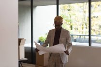 Smart businessman holding blueprint in office — Stock Photo