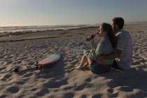 Jeune couple ayant une bière sur la plage — Photo de stock