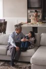 Grand-père et petite-fille interagissant les uns avec les autres sur le canapé dans le salon à la maison — Photo de stock