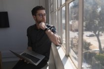 Мужчина руководитель смотрит в окно во время использования ноутбука в офисе — стоковое фото