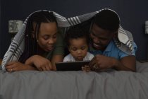 Сім'я, використовуючи мобільний під простирадлом, лежить на ліжку вдома — стокове фото