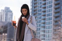 Hijab femmes prendre un café froid tout en utilisant un téléphone mobile — Photo de stock