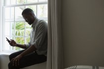 Homem usando telefone celular em uma sala de estar perto da janela — Fotografia de Stock