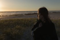 Mulher atenciosa de pé na praia durante o pôr do sol — Fotografia de Stock