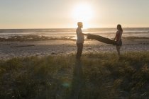 Coppie che tengono coperta sulla spiaggia durante il tramonto — Foto stock