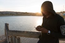 Athlète masculin utilisant un téléphone portable sur la jetée à la plage — Photo de stock