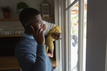 Отец с сыном на руках разговаривает по телефону дома — стоковое фото