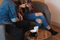 Baixa seção do casal usando telefone celular no café — Fotografia de Stock
