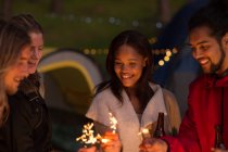 Group of friends having fun with sparklers at campsite — Stock Photo