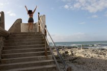 Rückansicht einer Joggerin, die mit erhobenen Armen in Strandnähe steht — Stockfoto