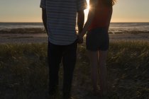 Baixa seção de casal de mãos dadas e de pé na praia — Fotografia de Stock