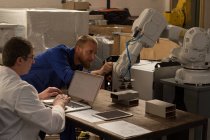 Robotic engineers examining robotic machine in warehouse — Stock Photo