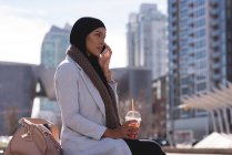 Женщина из хиджаба пьет холодный кофе, разговаривая по мобильному телефону в городе — стоковое фото