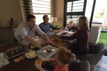 Семья, имеющая еду на обеденном столе в гостиной дома — стоковое фото