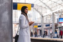 Hijab mujer esperando el tren mientras usa el teléfono móvil en la estación de tren - foto de stock