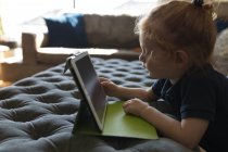 Вид сбоку на девочку, использующую цифровой планшет в гостиной дома — стоковое фото