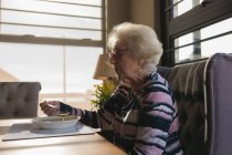 Vue latérale de la femme âgée ayant à manger à la maison — Photo de stock
