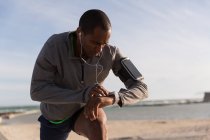 Atleta maschio che controlla il suo smartwatch mentre si esercita vicino alla spiaggia — Foto stock