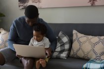 Отец и сын используют ноутбук в гостиной на дому — стоковое фото