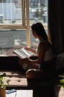 Mulher lendo livro no sofá na sala de estar em casa — Fotografia de Stock