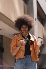 Frau trinkt Kaffee, während sie in der Stadt Musik auf dem Handy hört — Stockfoto