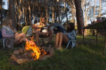Grupo de amigos se divertindo perto de fogueira no acampamento — Fotografia de Stock
