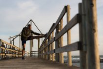 Male athlete stretching on pier at beach — Stock Photo