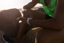 Mid section of male athlete using smartwatch near beach — Stock Photo