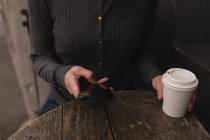 Средняя секция женщины с помощью мобильного телефона в кафе на открытом воздухе — стоковое фото