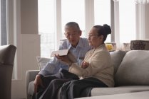 Seniorenpaar diskutiert über digitales Tablet auf Sofa im heimischen Wohnzimmer — Stockfoto