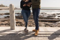 Sección baja de pareja discutiendo en el teléfono móvil en el paseo marítimo - foto de stock