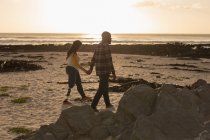 Couple holding hands and walking on beach during sunset — Stock Photo