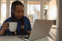 Mulher usando laptop na cozinha enquanto toma café em casa — Fotografia de Stock