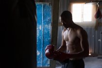 Без сорочки чоловічий боксер стоїть з боксерськими рукавичками в боксерському клубі — стокове фото
