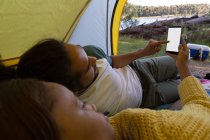 Young couple using mobile phone in tent at campsite — Stock Photo