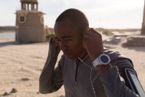 Atleta masculino usando fone de ouvido perto da praia em um dia ensolarado — Fotografia de Stock