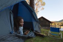 Femme utilisant un téléphone portable en tente au camping — Photo de stock