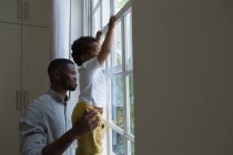 Padre e hijo de pie cerca de la ventana en casa - foto de stock