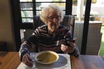 Seniorin benutzt Handy beim Essen zu Hause — Stockfoto