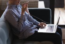 Executivo masculino falando no celular enquanto usando laptop no escritório — Fotografia de Stock