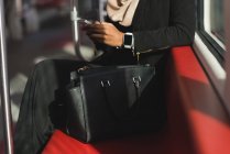 Sección media de la mujer que usa el teléfono móvil mientras viaja en tren - foto de stock