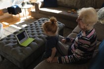 Бабушка и внучка делают видеозвонок на цифровой планшет в гостиной дома — стоковое фото