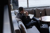 Uomo d'affari che beve whisky mentre utilizza tablet digitale in hotel — Foto stock