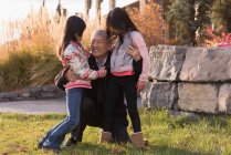 Feliz abuelo abrazando a sus nietas en un día soleado - foto de stock