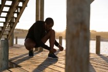 Male athlete tying his shoelaces on pier at beach — Stock Photo