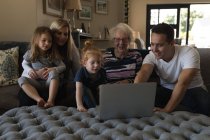 Родина багатьох поколінь використовує ноутбук на дивані у вітальні вдома — стокове фото