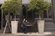 Belle femme utilisant un téléphone mobile tout en prenant un café dans un café extérieur — Photo de stock