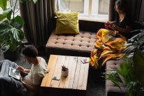 Couple utilisant téléphone portable et tablette numérique tout en prenant un café dans le salon à la maison — Photo de stock