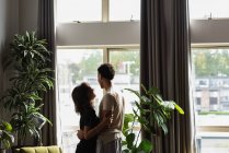 Casal olhando através da janela na sala de estar em casa — Fotografia de Stock